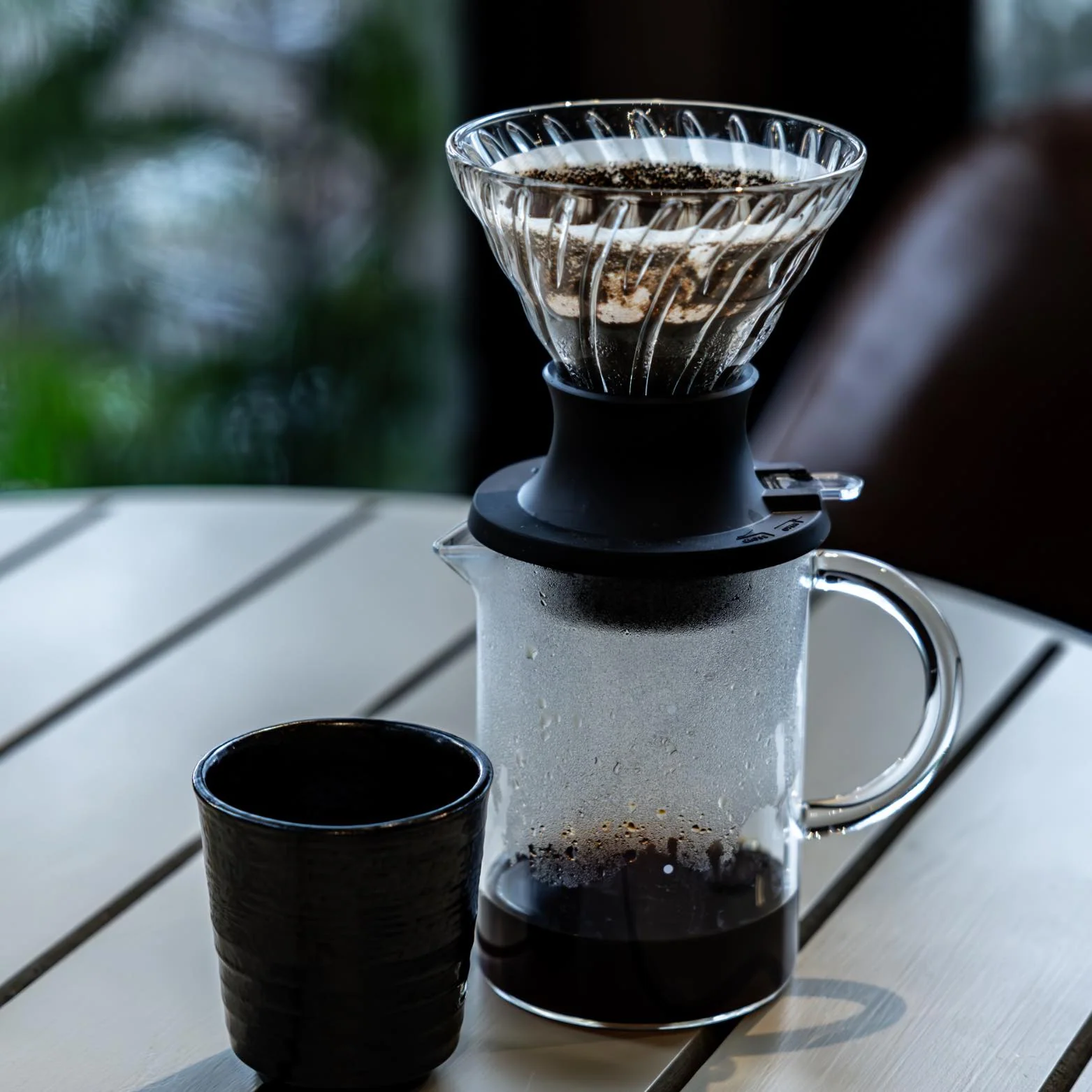 Coffee dripper above a glass server beside a small cup